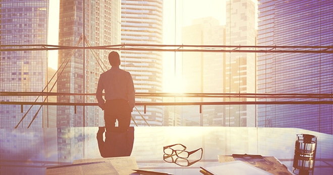 businessman looks out at sunrise from office