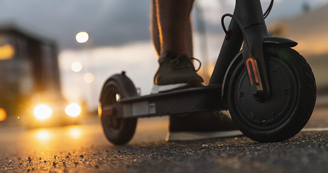 E scooter on road at dusk with car headlights in the background