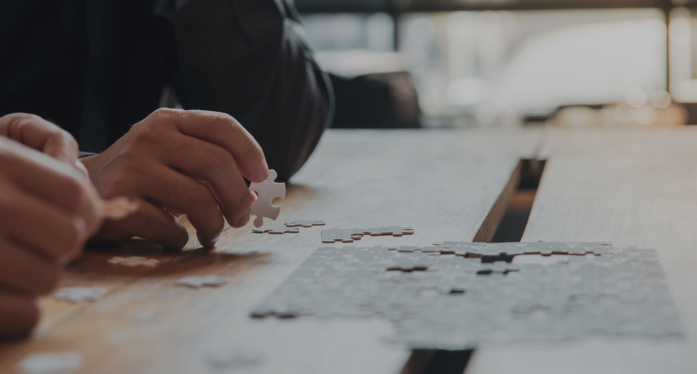 Man's hand holding a jigsaw piece whilst he's sat at a table putting an incomplete jigsaw puzzle together