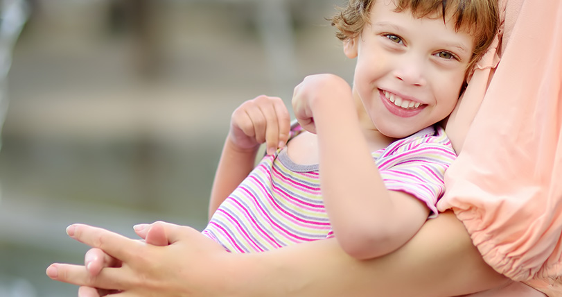 Child with cerebral palsy smiles at the camera whilst sitting in their mother's arms