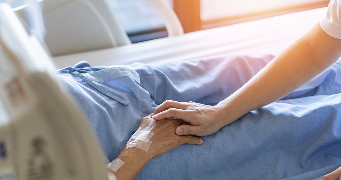 Person in hospital bed with woman touching their hand